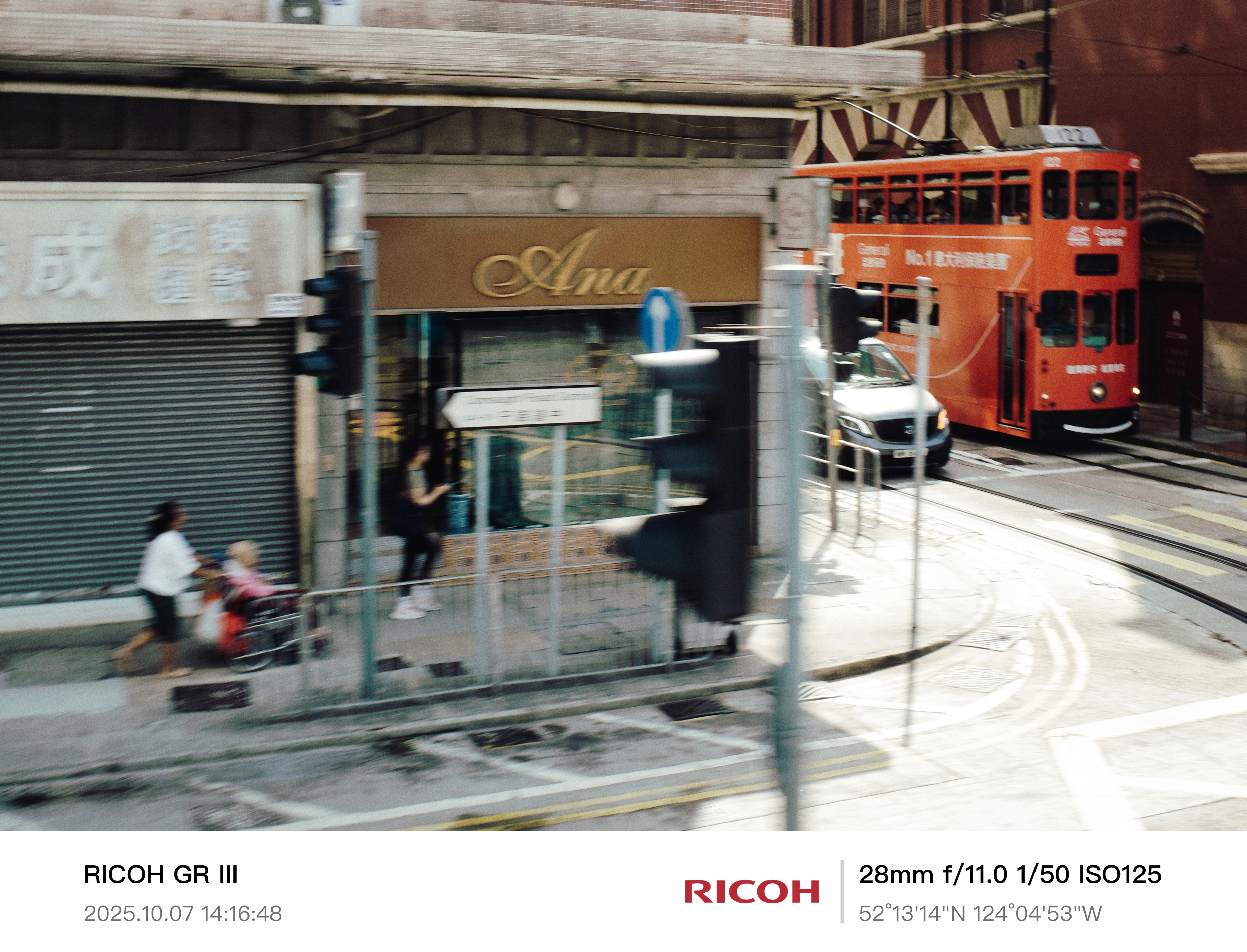 2025 - City in Motion - HK
《電車經過的街角》
拍摄于香港岛。
一辆红色电车穿过老旧的街道，人们行色匆匆。
时间裹挟着每一个人在城市涌动。